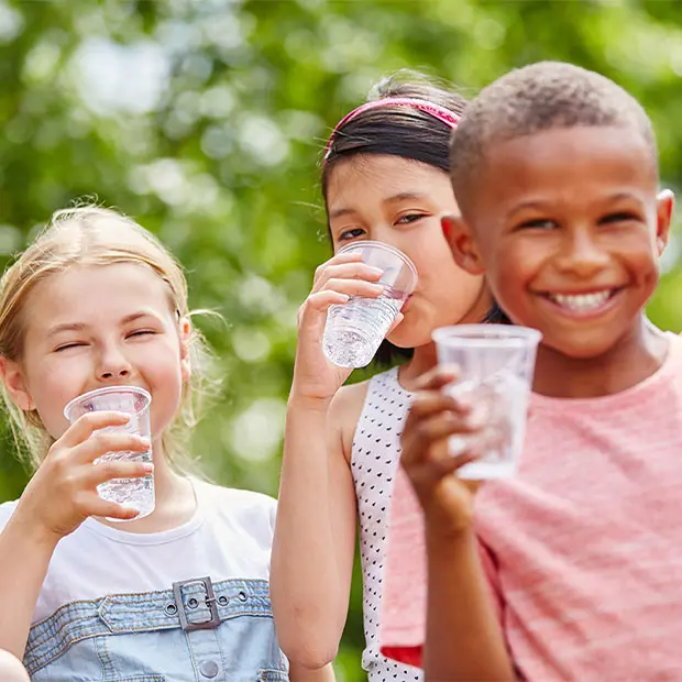 Children smiling while drinking water from plastic cups.