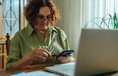 A woman checking her phone and trying to make a bill payment with her credit card.