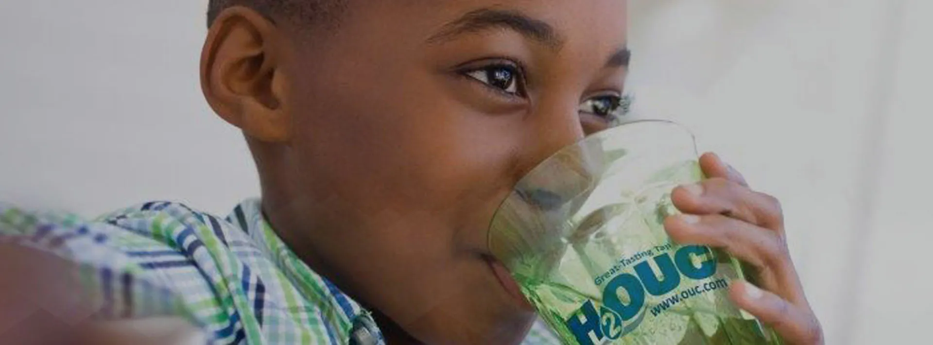 Boy drinking H2OUC water from a glass.