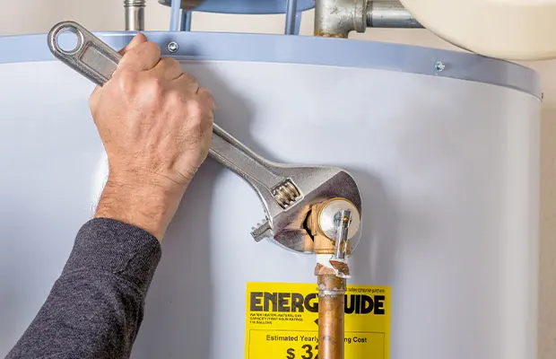 Hand holding a wrench, shown tightening a screw on a water heater line