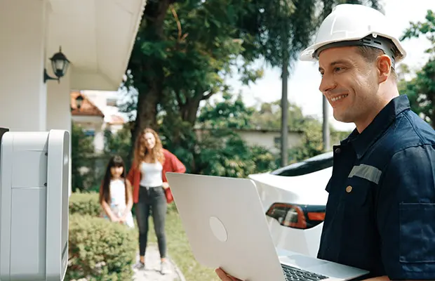 A technician holding a laptop and looking at an at-home EV charger