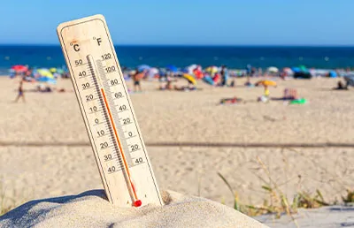 A thermometer in the sand on a beach, showing hot temperatures.