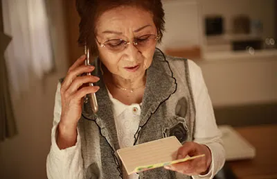 An elderly woman on the phone, looking at her checkbook. She is being asked to make a payment over the phone.