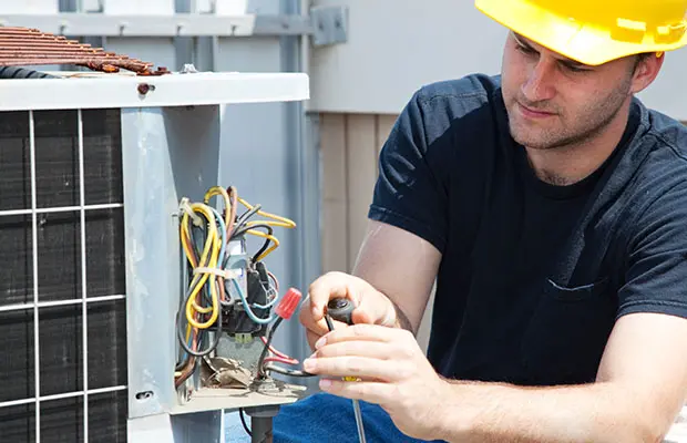 An HVAC repair technician working outside on a unit.
