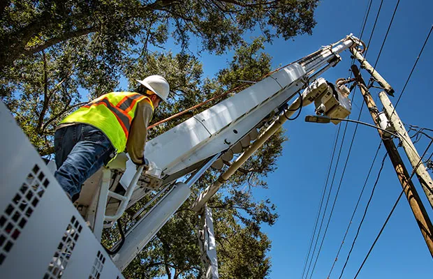 A utility employee looks up to monitor another employee as he repairs a powerline. 