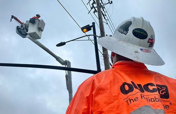 An OUC employee monitoring another employee making repairs on a power line.