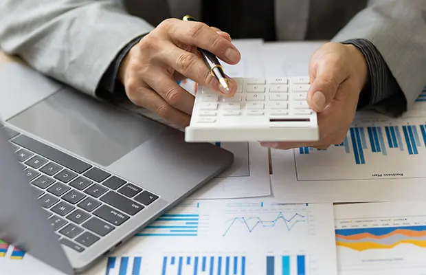 Man holding a calculator over a pile of papers displaying charts