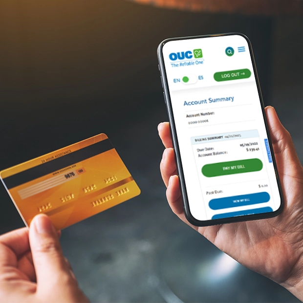 Hands holding a credit card and a cell phone open to myOUC's account summary
